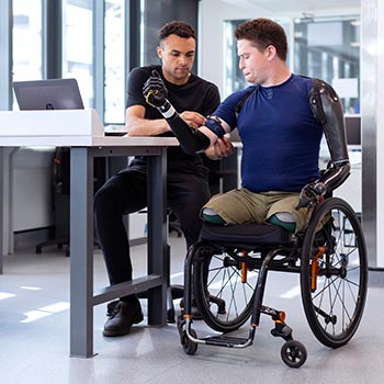 man in wheelchair with another man helping him affix a band to his arm