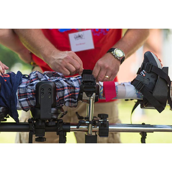 male caregiver using the leg straps on male child harnessed in the Prime Engineering Superstand HLT Pediatric Standing Frame
