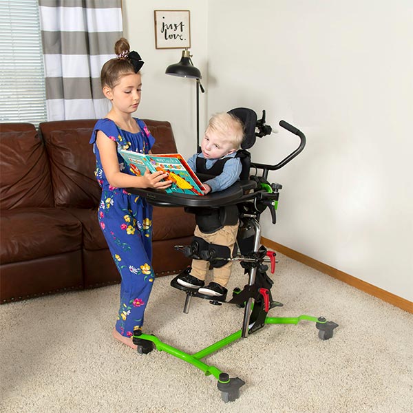Zing Multi-Positional Pediatric Standing Frame used by a child with disabilities as an elder sibling reads to them.